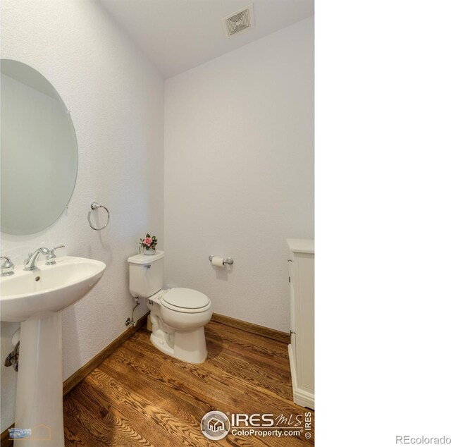 half bath featuring visible vents, toilet, a sink, wood finished floors, and baseboards