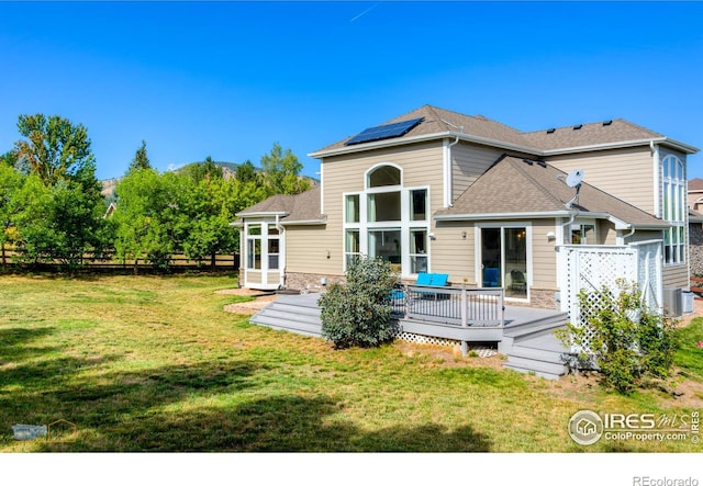 back of property with a wooden deck, solar panels, fence, cooling unit, and a yard