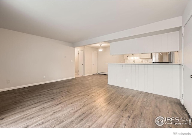 unfurnished living room with a baseboard heating unit, baseboards, and light wood-style floors