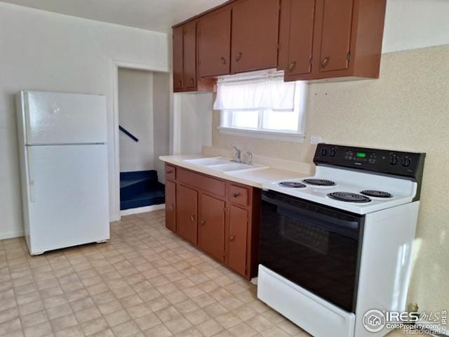 kitchen with range with electric cooktop, a sink, light countertops, freestanding refrigerator, and brown cabinets