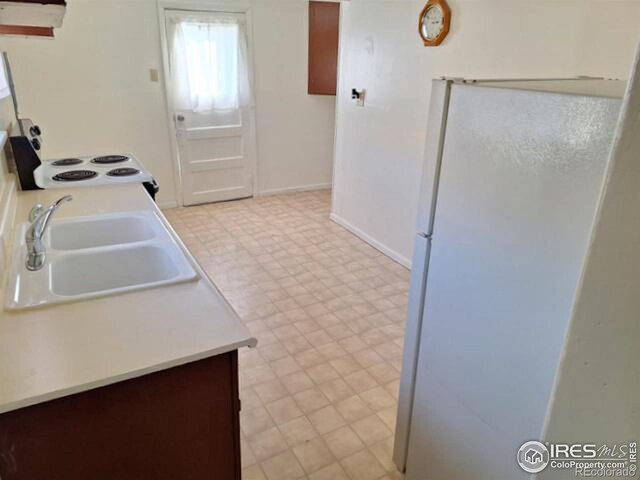 kitchen with light floors, light countertops, electric range, freestanding refrigerator, and a sink