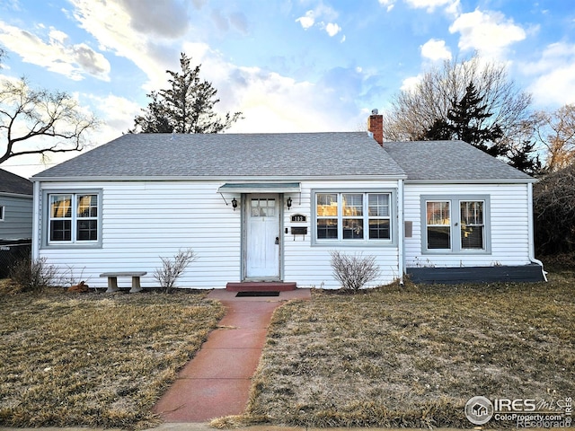 ranch-style home with a front lawn, a chimney, and a shingled roof