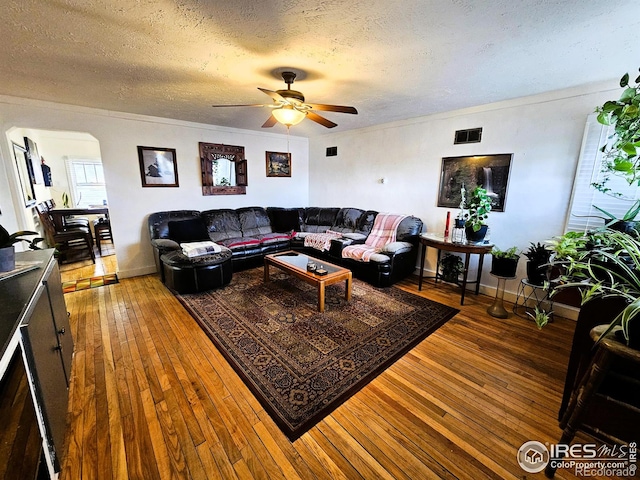 living room with arched walkways, hardwood / wood-style floors, ornamental molding, and visible vents