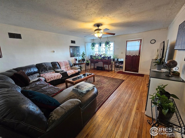 living room featuring a ceiling fan, visible vents, light wood-style flooring, and a textured ceiling