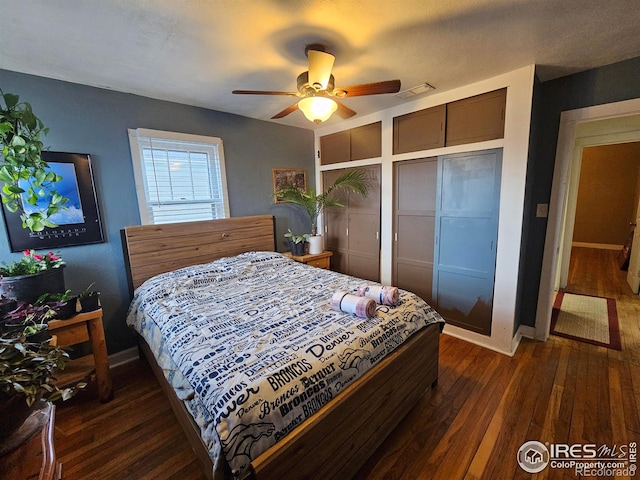 bedroom featuring two closets, dark wood finished floors, visible vents, and baseboards