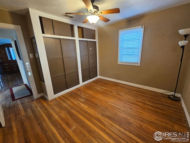 unfurnished bedroom featuring baseboards, visible vents, a ceiling fan, dark wood-style floors, and a closet