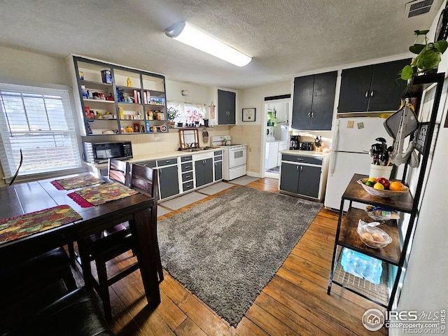 kitchen featuring white appliances, dark cabinetry, visible vents, and light wood finished floors