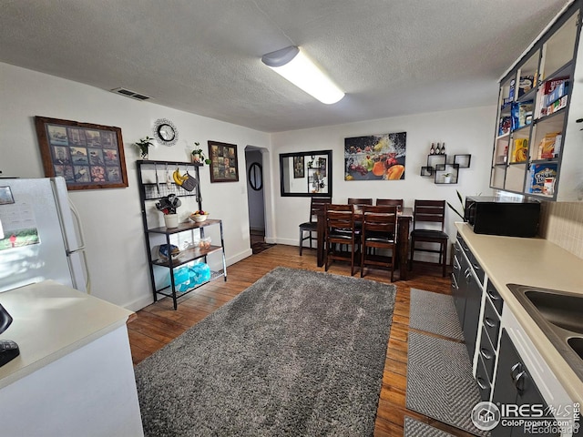 dining space with a textured ceiling, dark wood-type flooring, visible vents, and baseboards