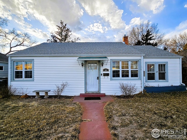 ranch-style home with a shingled roof, a chimney, and a front lawn