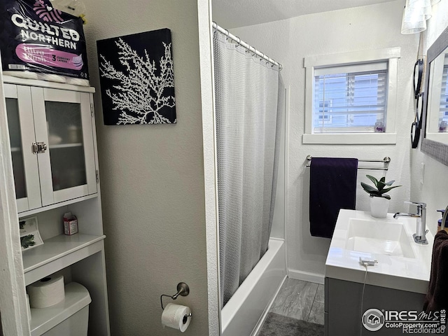 bathroom featuring toilet, a textured wall, shower / bathtub combination with curtain, and vanity