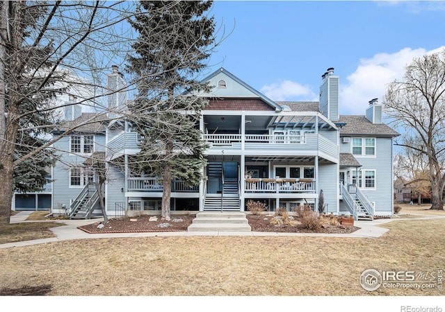 view of front of house featuring a chimney, roof with shingles, stairway, and a front yard