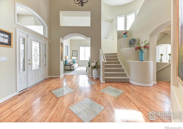 entryway featuring arched walkways, a towering ceiling, baseboards, stairs, and light wood-style floors