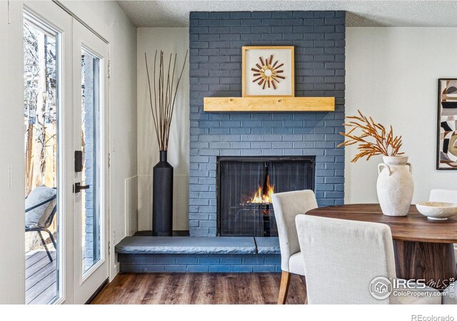 living area with a textured ceiling, french doors, a brick fireplace, and dark wood finished floors