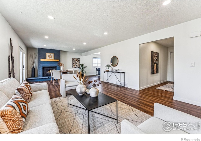 living room featuring a textured ceiling, recessed lighting, wood finished floors, baseboards, and a brick fireplace