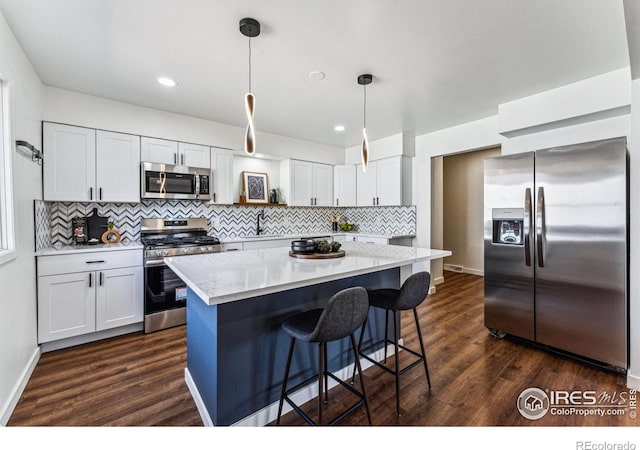 kitchen with appliances with stainless steel finishes, dark wood-type flooring, a center island, hanging light fixtures, and white cabinetry