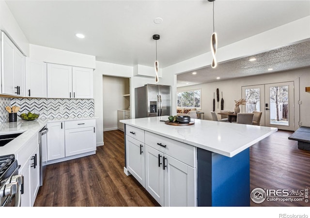 kitchen with pendant lighting, french doors, stainless steel appliances, white cabinetry, and a kitchen island