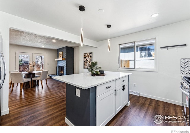 kitchen with a kitchen island, white cabinets, hanging light fixtures, light stone countertops, and dark wood finished floors