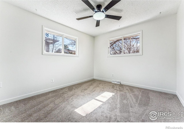 carpeted spare room with visible vents, a textured ceiling, baseboards, and a wealth of natural light