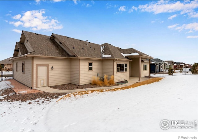 snow covered property featuring fence and roof with shingles