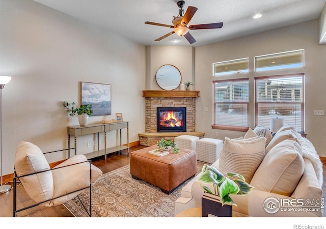 living area featuring ceiling fan, a stone fireplace, recessed lighting, wood finished floors, and baseboards