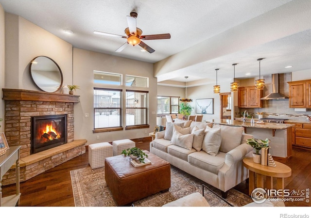 living room featuring dark wood-style floors, a fireplace, a ceiling fan, and a textured ceiling