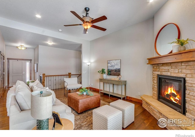 living room with a ceiling fan, a stone fireplace, baseboards, and wood finished floors