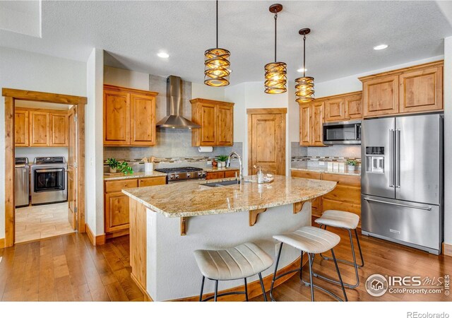 kitchen featuring a kitchen island with sink, separate washer and dryer, a sink, high quality appliances, and wall chimney range hood