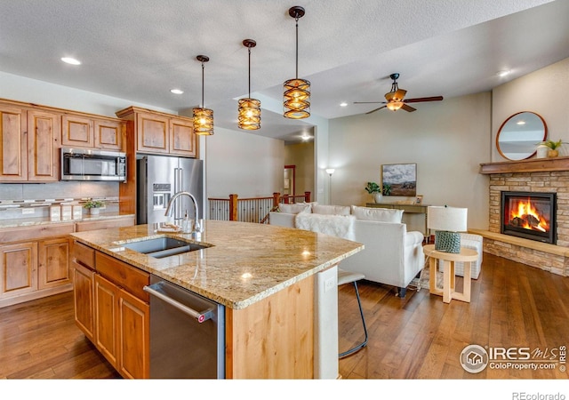 kitchen with dark wood-style floors, stainless steel appliances, open floor plan, a sink, and an island with sink