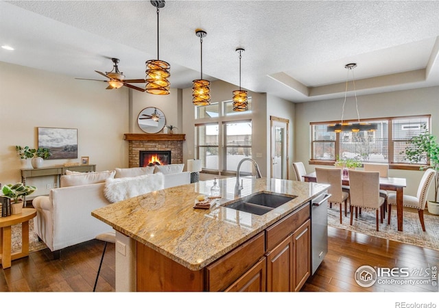 kitchen with a kitchen island with sink, a sink, decorative light fixtures, and light stone countertops