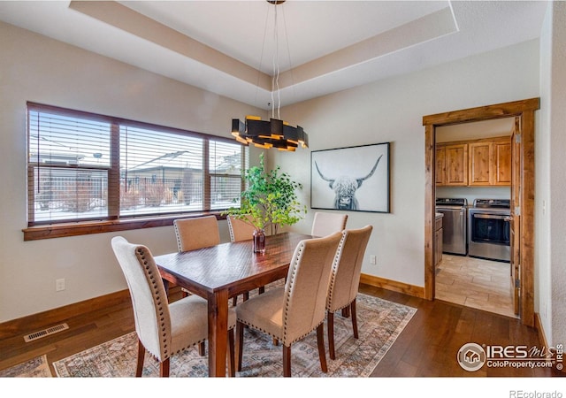 dining room featuring a tray ceiling, dark wood-style flooring, washing machine and clothes dryer, visible vents, and baseboards