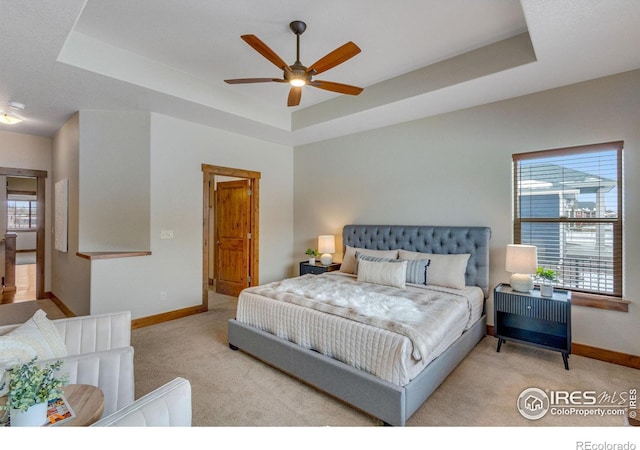 bedroom featuring a raised ceiling, light carpet, and baseboards