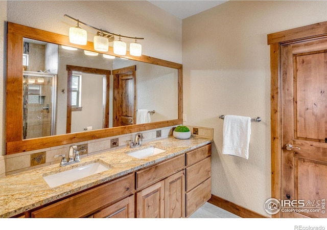 full bath with double vanity, a shower stall, baseboards, and a sink