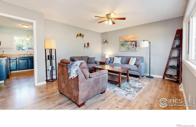 living room featuring a ceiling fan, light wood-style flooring, baseboards, and a textured ceiling