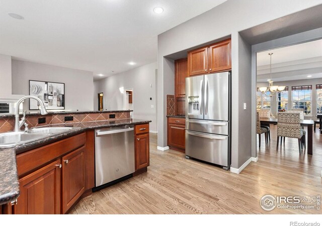 kitchen with light wood finished floors, decorative backsplash, an inviting chandelier, stainless steel appliances, and a sink