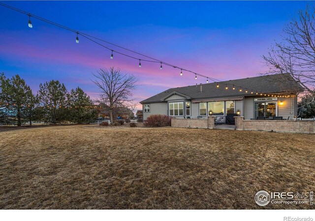 back of house at dusk with brick siding, a lawn, and a patio area