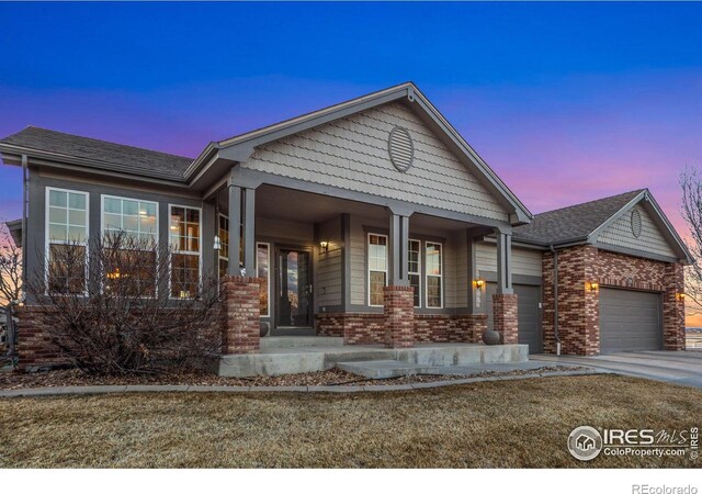 view of front facade with a porch, an attached garage, brick siding, concrete driveway, and a lawn