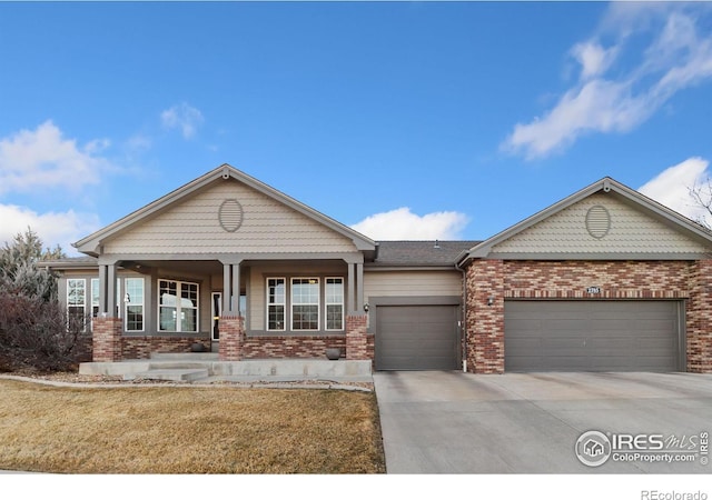 view of front of home featuring driveway, brick siding, an attached garage, covered porch, and a front yard