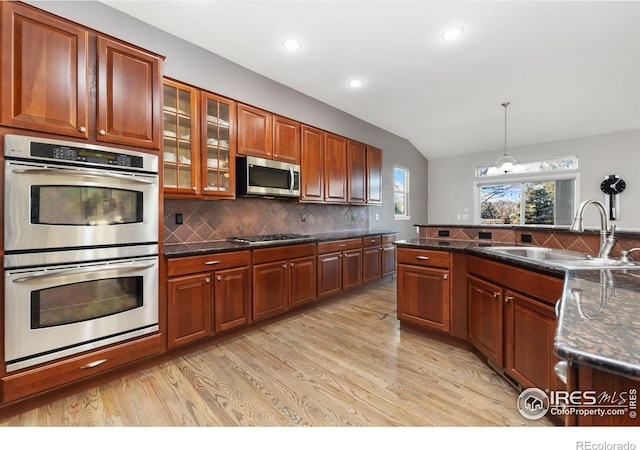 kitchen with decorative light fixtures, decorative backsplash, appliances with stainless steel finishes, glass insert cabinets, and a sink