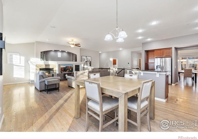 dining space featuring recessed lighting, ceiling fan with notable chandelier, baseboards, light wood finished floors, and a glass covered fireplace