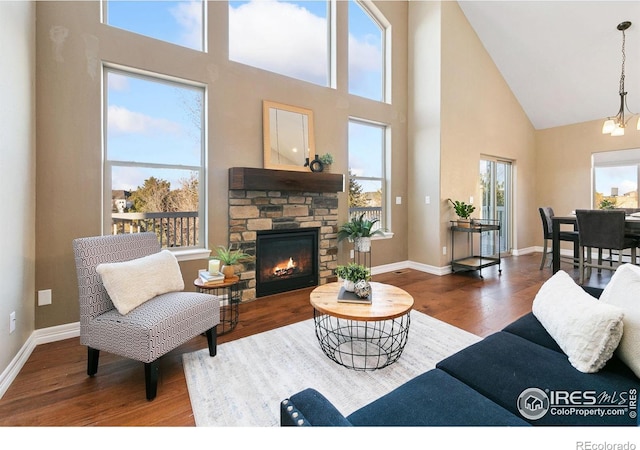 living room with high vaulted ceiling, baseboards, wood finished floors, and a stone fireplace