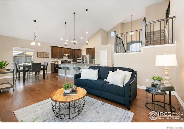 living room featuring an inviting chandelier, baseboards, dark wood-style floors, and high vaulted ceiling