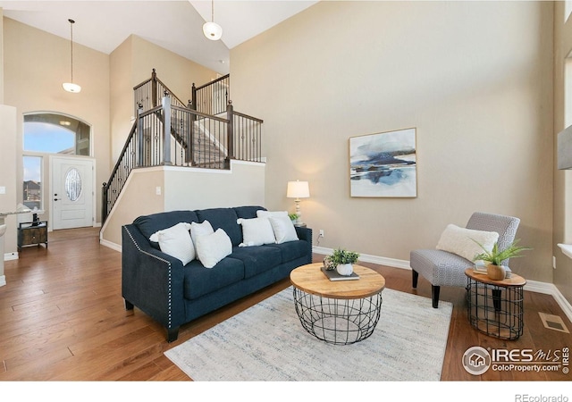 living room featuring dark wood-style flooring, visible vents, a high ceiling, baseboards, and stairs