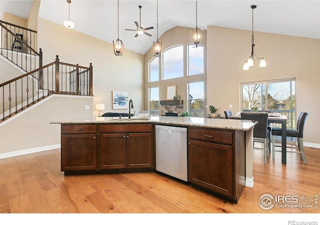 kitchen with decorative light fixtures, a center island with sink, stainless steel dishwasher, a sink, and light wood-type flooring