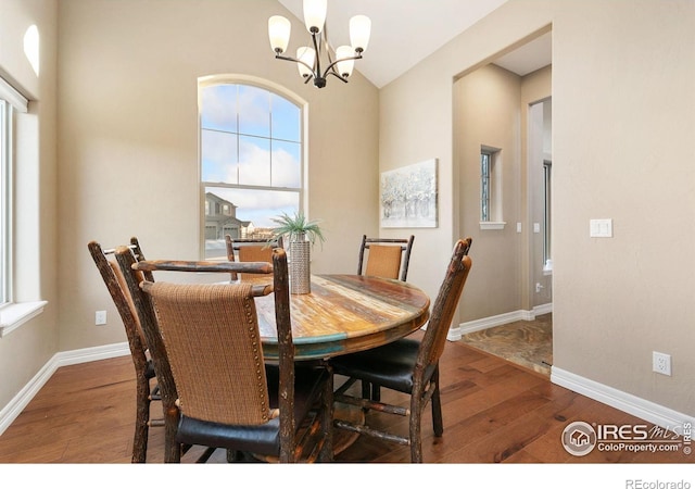 dining space with a notable chandelier, lofted ceiling, hardwood / wood-style flooring, and baseboards