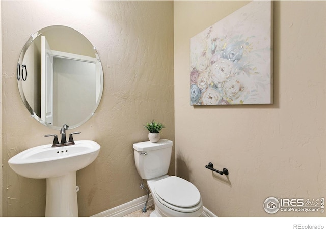 half bath featuring toilet, baseboards, and a textured wall