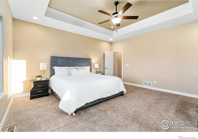 carpeted bedroom featuring a raised ceiling, visible vents, and baseboards