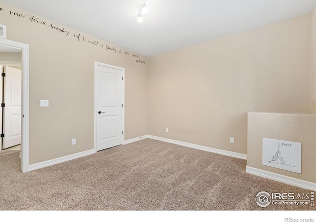 carpeted empty room featuring track lighting, visible vents, and baseboards