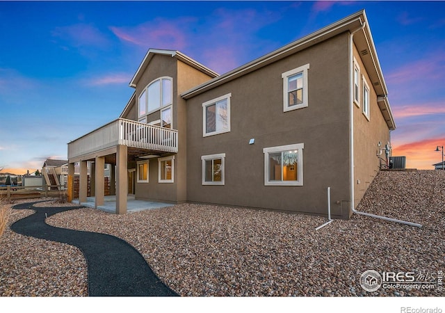 back of house at dusk with cooling unit, a patio, and stucco siding