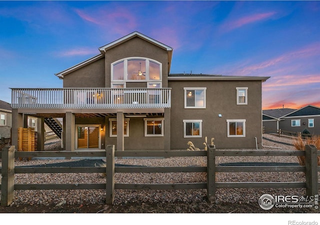 back of house at dusk with a deck, a fenced front yard, stairs, and stucco siding