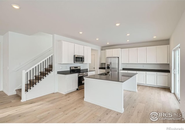 kitchen with stainless steel appliances, dark countertops, a center island with sink, and a sink